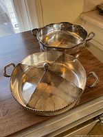 Both silver serving dishes side by side on wooden surface showing overall shape and handles