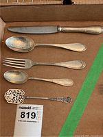 All five flatware pieces laid out: knife, two spoons, fork, and pierced serving utensil. Shows scale and condition.