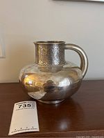 Full front view of silver pitcher showing bulbous body, neck engraving and handle