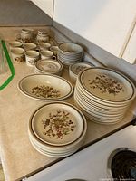 Photo showing stacked plates, cups, saucers, cream and sugar set, serving bowl in Gaiety floral pattern stoneware.