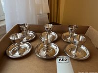Set of 6 silver plate egg cups with matching saucers placed in a cardboard box on a table near window
