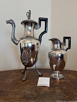Front view of coffee pot on tripod legs alongside matching creamer jug