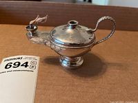 Side view of small sterling silver oil lantern showing spout with wick, lid, and snake-shaped handle.