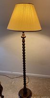 Full view of the solid wood floor lamp illuminated, showing the turned wooden column and pleated beige lampshade.