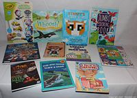 Photo showing 11 children's books and activity books arranged on a white surface with colorful covers, including Crayola sticker and coloring books, storybooks, and themed activity books.