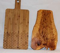 Photo of two cutting boards side by side, bamboo with handle and engraved pattern, and natural wood slab board.