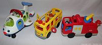 Three Fisher Price musical interaction vehicles including an airplane, school bus, and fire truck arranged side by side on white surface against white background.