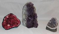 Three geodes arranged on a plain background showing color and size differences between pink and amethyst quartz geodes