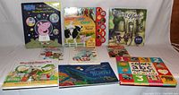 Photo of 9 children's books arranged in two rows on a white surface including Peppa Pig, farm animal sounds book, Where's the Knight puzzle book, Munschworks, and educational books.