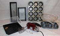 Photo showing Betty Crocker red hand mixer with beaters and dough hooks, two rectangular bread pans, cupcake and muffin pans, cooling racks, and a round glass baking dish with wire rack and stand.