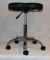 Front view of black swivel stool showing padded seat, height adjustment lever, chrome base, and caster wheels.