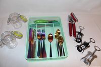 Image showing iridescent cutlery in a mint green plastic tray, three wine openers with red and black handles, and two glass storage jars with latch lids.