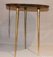 Front view of the handmade brass side table showing round top and three legs with hammered finish