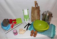 Photo of kitchen items arranged on white surface including side strainer, composter, cutting board, bowl, salt and pepper shakers, and other kitchen tools.