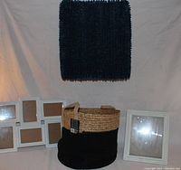 Laundry basket surrounded by two white picture frames with blue rug in background