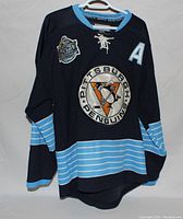 Front view of black Pittsburgh Penguins hockey jersey with Winter Classic patch, large team logo, and light blue striped design.