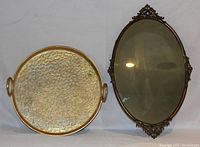 Photo showing the round decorative metal platter with textured golden surface and handles beside the oval mirror with ornate metal frame.
