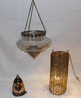 Photo of a Moroccan hanging glass lantern with metal detailing suspended by chains next to a lit wicker cylindrical lamp with power cord.