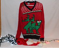 Full view of the sweater, Santa hat, and two sets of string lights, one white and one multicolored, arranged on neutral background.