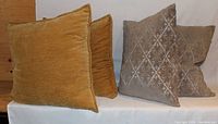 Two mustard yellow and two gray diamond pattern throw pillows arranged standing on a white surface, showing front sides.