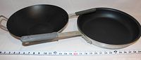 Photo showing a black wok and a 14-inch commercial fry pan side by side with a measuring scale underneath.
