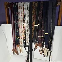 Photo showing 15 sets of men's button suspenders hanging on rack, various patterns and colors visible.