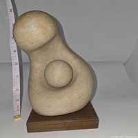 Front view of the stone mother and child sculpture with measuring tape showing height approx 7 inches.