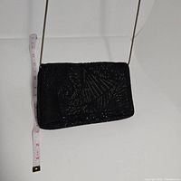 Black beaded evening bag with a geometric bead pattern shown hanging by its thin metallic shoulder strap, with measuring tape beside it to show size approximately 5 inches in height and 8 inches in width.
