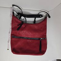 Front view showing red leather, front zipper pocket with black leather pull, Calvin Klein logo, and black adjustable shoulder strap with silver hardware, measuring tape for size reference.