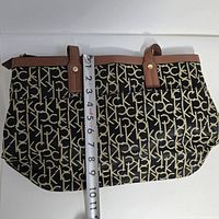 Calvin Klein tote bag with a tape measure showing about 10 inches height, black and beige signature CK monogram canvas, brown leather trim and handles.
