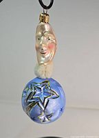 Front view of ornament highlighting the hand-painted moon face and the blue globe with star decorations.