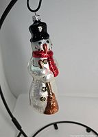 Front view of Christopher Radko snowman ornament showing black top hat, face, red scarf, buttons, and broom.