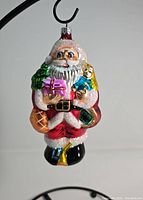 Front view of the Santa Claus glass ornament with gifts and doll showing color and glitter details.