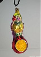 Front view of Christopher Radko glass bird ornament with yellow, pink, and green coloring perched on red reflector showing detailed textures.