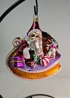 Front view of Christopher Radko glass Santa Claus ornament on a sleigh with colorful presents and a teddy bear