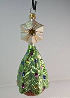 Front view of green Christmas tree ornament with colorful gemstone decorations and gold star topper with cap and loop for hanging.