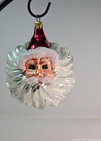Front view of the Christopher Radko Santa face glass ornament, showing detailed facial features and glitter accents on beard and hat.