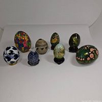 All eight decorative eggs arranged in single row showing designs and stands.