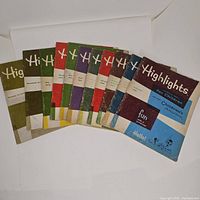 Front view of eleven Highlights magazines for children with colorful covers, arranged in a fan shape showing the range of years and colors.