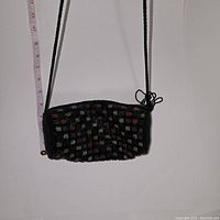 Front view of the black beaded cylindrical evening bag with multicolored small square bead patterns and a single long strap, measuring approximately 7 inches in length.