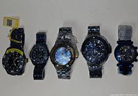 Front view of all five Invicta watches laid flat side by side showing variety