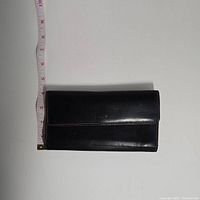 Top view of closed black leather wallet with measuring tape showing length just over 7 inches.