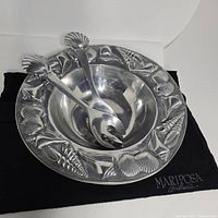 Salad bowl with shell design border, the matching fork and spoon resting inside. Black felt storage bag with embroidered logo underneath.