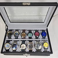 Top view of 12 watches in display box showing dials and colors.