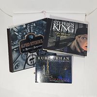 Three literature-themed pop-up books stacked on a white surface: 'Alfred Hitchcock: The Master of Suspense,' 'Stephen King: The Girl Who Loved Tom Gordon,' and 'Kubla Khan.'