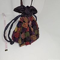 Close-up image of the Thai silk drawstring bag showing multicolored circular fabric pieces and drawstring strap, with measuring tape nearby indicating size.