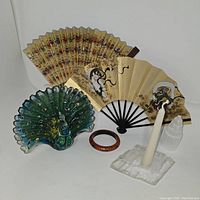 Group photo showing all items: glass peacock figurine, two decorative fans, selenite candle holder with candle, selenite tower, and red bangle bracelet.