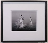 Full view of the framed and matted black-and-white photographic print showing two figures entering the water, the image is centered within a large white mat and black frame.
