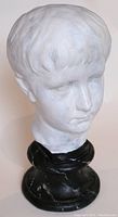 Front-right angled view of plaster head sculpture mounted on black faux marble plinth, showing facial details and hair texture.