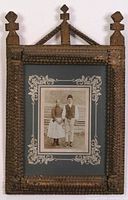 Full view of ornate carved wood frame holding vintage sepia portrait of couple in traditional Eastern European dress.